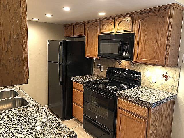 Kitchen at Emerald Cove with wood cabinets, granite-look countertops, tile backsplash and black appliances