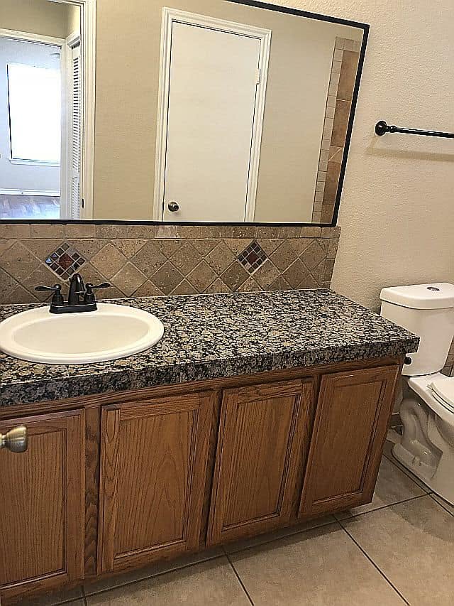 Bathroom at Emerald Cove with a stone-look vanity countertop, framed mirror and tile backsplash